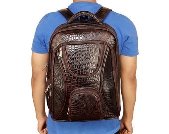 Pode incluir: Uma mochila de couro marrom com textura de pele de crocodilo. A mochila tem vários compartimentos com zíper, uma alça superior e alças de ombro ajustáveis. A pessoa na imagem está vestindo uma camiseta azul.