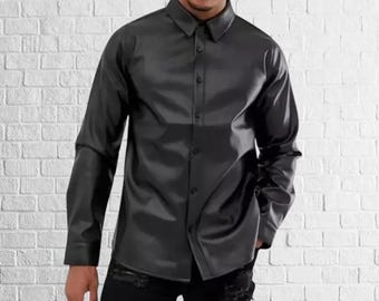 May include: A black button-down shirt with long sleeves. The shirt is made of a shiny, leather-like material. The collar is pointed, and the shirt is buttoned up. The background is a white brick wall.