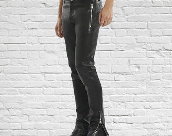 May include: Black leather pants with a slim fit and zippered details. The pants have a classic five-pocket design and a zipper closure. The model is wearing black leather boots. The background is a white brick wall.
