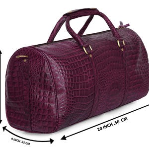 May include: A deep purple duffel bag with a crocodile skin texture. The bag has two handles and gold-colored hardware. It measures 20 inches long, 13.5 inches high, and 9.25 inches wide.