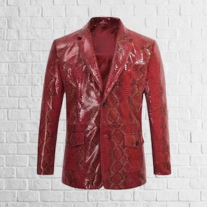 Puede incluir: Un blazer rojo con estampado de piel de serpiente, con cierre de dos botones y dos bolsillos delanteros. La chaqueta tiene solapas con muescas y mangas largas. El blazer está hecho de un material brillante, sobre una pared de ladrillos blancos.