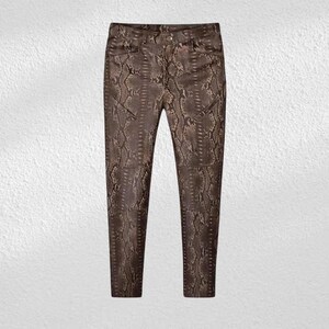 May include: Brown faux leather trousers featuring a snakeskin print. The trousers have a classic five-pocket design and a button and zip fastening. The neutral colour allows for versatile styling with various tops.