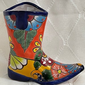 May include: A colourful ceramic boot with a floral design. The boot is painted in shades of red, yellow, blue, green, and white. The boot is a decorative item and can be used as a vase or planter.