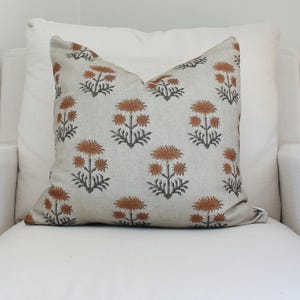 Könnte beinhalten: Ein beiger Kissenbezug mit einem floralen Muster in Braun- und Orangetönen. Das Kissen hat eine dezente Leinenstruktur.
