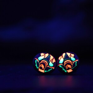 May include: A pair of glow-in-the-dark earrings with a floral design in shades of green, orange, and blue.