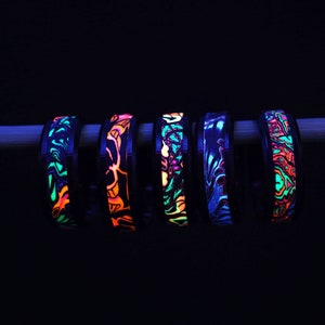 May include: Six black rings with colourful glow-in-the-dark patterns. The rings are arranged in a row and are illuminated with a blacklight.