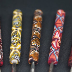 Può includere: Cinque strumenti colorati con punte metalliche. Gli strumenti sono realizzati in pasta polimerica e presentano disegni intricati in tonalità di rosso, arancione, giallo, bianco e nero.