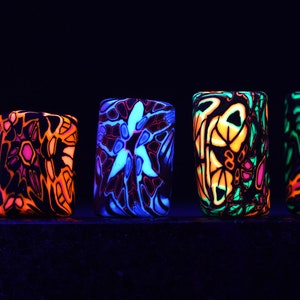 May include: Five colourful, geometrically patterned, rectangular blocks glowing under a blacklight. The blocks are made of a translucent material and have a variety of colours, including blue, green, orange, pink, and yellow.