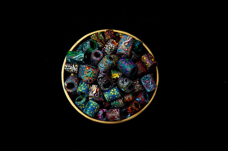 May include: A bowl filled with colorful, patterned, cylindrical beads. The beads are made of polymer clay and have a variety of designs, including floral, geometric, and abstract patterns. The beads are arranged in a random order, creating a visually appealing and eclectic display.