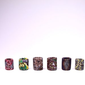 May include: Eight colorful cylindrical beads with intricate patterns. The beads are made of polymer clay and have a variety of colors, including red, blue, green, yellow, and brown.