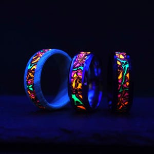 May include: Three glow-in-the-dark rings with colorful patterns. The rings are made of wood and metal and are stacked on top of each other.