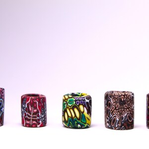 May include: Five colorful cylindrical beads with intricate patterns. The beads are made of polymer clay and feature a variety of colors, including red, blue, green, yellow, and brown.