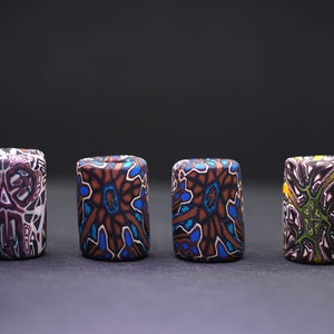 May include: Six colorful cylindrical beads with intricate geometric patterns. The beads are made of polymer clay and have a variety of colors, including brown, blue, green, yellow, and white.