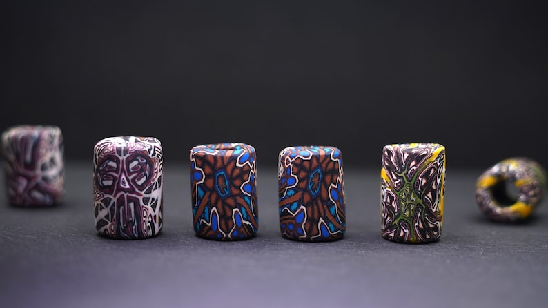 May include: Six colorful cylindrical beads with intricate geometric patterns. The beads are made of polymer clay and have a variety of colors, including brown, blue, green, yellow, and white.