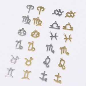May include: A set of 12 silver and gold zodiac sign charms. The charms are in the shape of the astrological signs: Aries, Taurus, Gemini, Cancer, Leo, Virgo, Libra, Scorpio, Sagittarius, Capricorn, Aquarius, and Pisces.