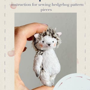 Op de afbeelding: Een wit en grijs stekelig knuffeldier, 8,5 cm hoog, met een PDF-patroon en instructies om te naaien.