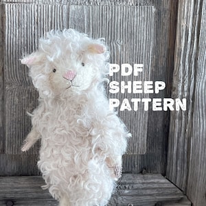 Op de afbeelding: Een handgemaakt wit schapenknuffel met krullend haar, roze oren en een roze neus. De tekst "PDF SHEEP PATTERN" staat in het wit. Het schaap staat op een lichtgroen oppervlak tegen een rustieke houten achtergrond.
