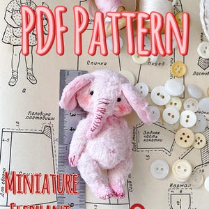 Op de afbeelding: Een roze miniatuur olifant knuffel, ongeveer 9 cm hoog, staat centraal. De tekst "PDF PATTERN" en "MINIATURE ELEPHANT" in het rood zijn zichtbaar. Knoppen en naaigerei zijn ook aanwezig.