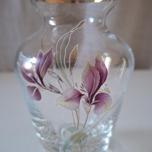 May include: A clear glass vase with a gold rim and a floral design. The vase features purple and white flowers with green leaves.