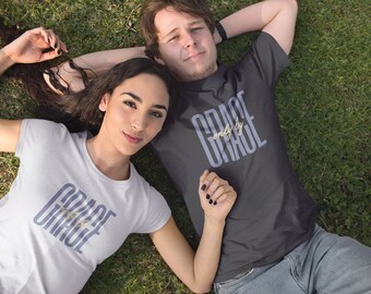 以下が含まれることがあります： 「GRACE only by GRACE」の文字がスタイリッシュなフォントでプリントされたTシャツを着た2人。片方のシャツは白、もう片方は濃いグレーです。緑の芝生の上に寝転んで、カメラを見上げています。