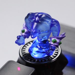 May include: A translucent blue figurine of a fantasy character with purple accents and green gems. The figure is posed with arms outstretched, atop a black and silver circular base. The base has a blue light emanating from it.
