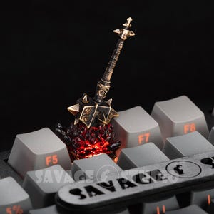 Könnte beinhalten: Ein detaillierter, miniaturisierter Streitkolben mit einem stacheligen Kopf und einem verzierten Griff, der auf einer Computertastatur ruht. Der Streitkolben hat goldene und schwarze Akzente, mit einem feurigen roten Glühen, das von seiner Basis ausgeht. Die Tastaturtasten sind grau.