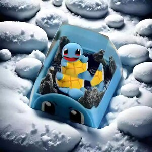 May include: A blue and yellow Squirtle figurine inside a blue container with a snowy background. The Squirtle figure has a yellow shell and a red mouth. The container has black accents and is surrounded by white snowballs.