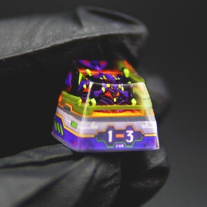 May include: A custom keycap with a vibrant design featuring purple, orange, green, and yellow accents. The keycap has the numbers "1-3" on the front. The keycap is likely for a mechanical keyboard.