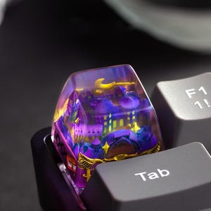 May include: A custom keycap with a miniature, colorful cityscape design. The keycap is transparent, with a purple, yellow, and blue townscape visible inside. The word "Tab" is printed on the adjacent key.
