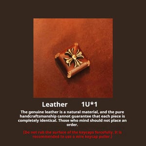 Può includere: Un copritasto quadrato in pelle marrone con un design a croce color oro al centro. Il copritasto ha bordi cuciti. L'immagine include la parola "Pelle" e il testo: "La vera pelle è un materiale naturale..."