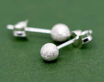 May include: A pair of silver stud earrings with a textured ball design. The earrings are on a green background.