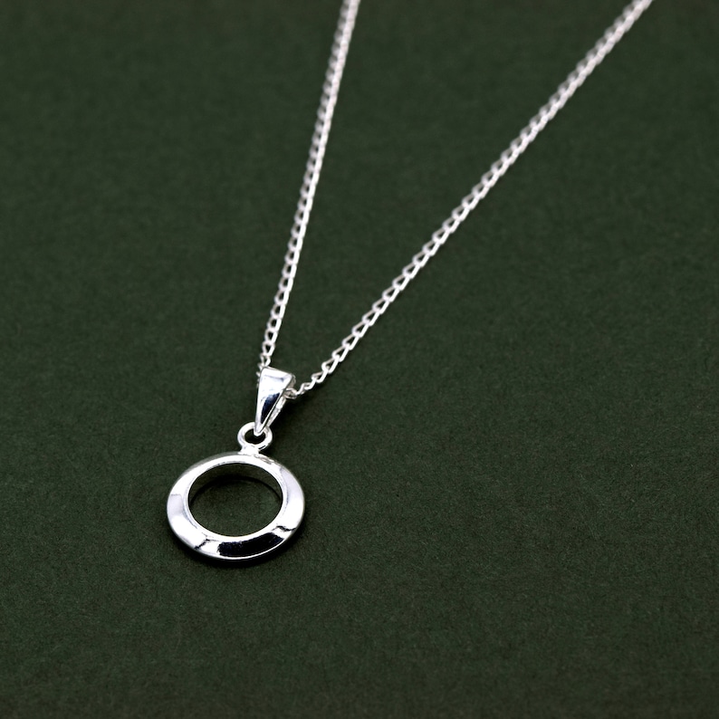May include: A silver chain necklace with a simple circle pendant. The pendant is smooth and has a slightly raised edge.
