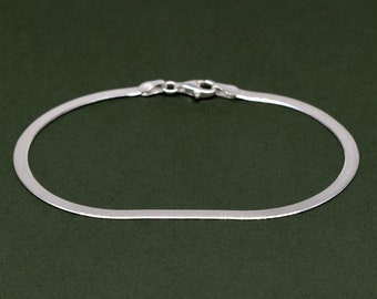 May include: A silver chain bracelet with a flat, rectangular design. The bracelet is made of a smooth, shiny metal and has a simple, elegant look.
