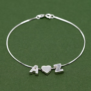 Könnte beinhalten: Ein silbernes Kettenarmband mit einem Herz-Anhänger und den Buchstaben A und Z.