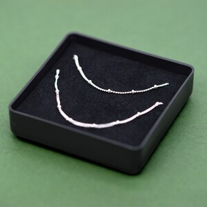 May include: Two silver necklaces with small beads, displayed in a black velvet-lined box.