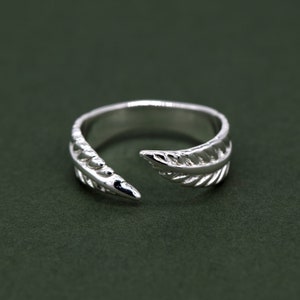 May include: A silver ring featuring a feather design. The ring is open on one side and has a delicate, detailed design.