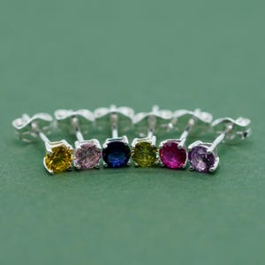May include: A set of six silver stud earrings with round gemstones in various colours, including yellow, pink, blue, green, red, and purple.