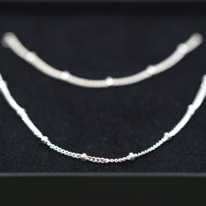 May include: Two silver necklaces with small round beads on a black background.