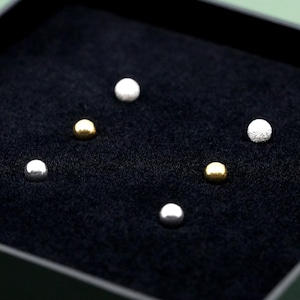 May include: Six small stud earrings in a variety of finishes, including silver and gold. The earrings are displayed on a black surface. Some have a textured appearance. These are likely for pierced ears.