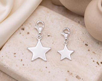 May include: Two silver-toned star charms, each featuring a smooth, polished surface and a secure lobster claw clasp. The charms are presented in two different sizes, with the larger star positioned to the left of the smaller star.