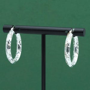 May include: Silver hoop earrings with a starburst design, displayed on a black stand against a green backdrop. The earrings are roughly 3.8 cm in diameter. A classic jewellery item.
