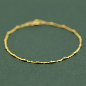 May include: A delicate gold chain bracelet with small beads spaced evenly along the chain.