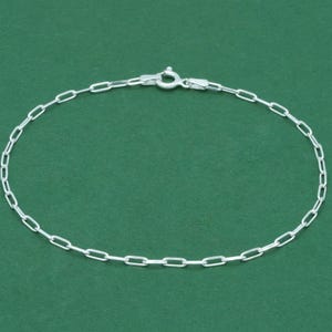 Peut inclure: Un bracelet délicat en chaîne d'argent avec un design à maillons ovales. Le bracelet est doté d'une fermeture à fermoir mousqueton. Le bijou est présenté sur un fond vert uni. Le bracelet mesure environ 17,78 cm de long.