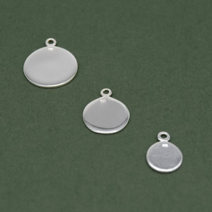 May include: Three silver blank round disc charms with a loop at the top. The charms are different sizes, with the largest charm at the top and the smallest charm at the bottom.
