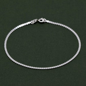 May include: A silver chain bracelet with a delicate, flat, oval-shaped link design.