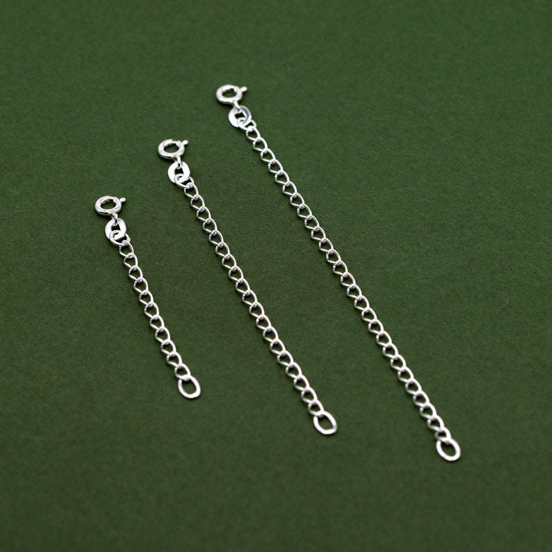 May include: Three silver chain extenders of different lengths on a green background.