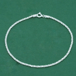 K&ouml;nnte beinhalten: Ein filigranes Silberarmband mit einem strukturierten, funkelnden Design. Das Armband verf&uuml;gt &uuml;ber einen sicheren Verschluss und wird vor einem einfarbigen gr&uuml;nen Hintergrund pr&auml;sentiert. Dieses Schmuckst&uuml;ck eignet sich f&uuml;r den Alltag oder besondere Anl&auml;sse.