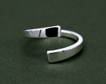 May include: A silver ring with a unique open design. The ring is made of a single piece of metal that is bent into a circle and then twisted to create a unique shape.