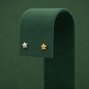 May include: A pair of stud earrings featuring a five-pointed star shape. One earring is finished in a polished silver tone, while the other earring is finished in a polished gold tone. Both star-shaped studs have a smooth, reflective surface.