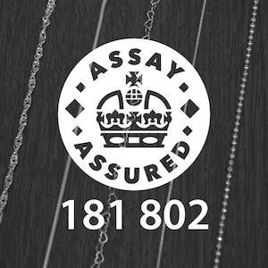 K&ouml;nnte beinhalten: Schwarz-wei&szlig;-Bild mit einem wei&szlig;en runden Emblem mit der Aufschrift "ASSAY ASSURED" und einem Kronen-Design. Darunter die Zahlen "181 802". Zarte Silberketten sind auf beiden Seiten des Emblems zu sehen.